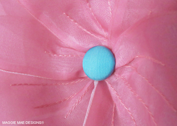 A teal silk-covered button forms the center of the floral trim on the "Cozmic One" hat