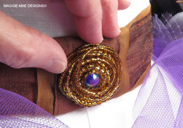 A one-of-a-kind chocolate/chestnut beaded brooch with plum purple center adorns the back seam of the "I'll Have Another" hat